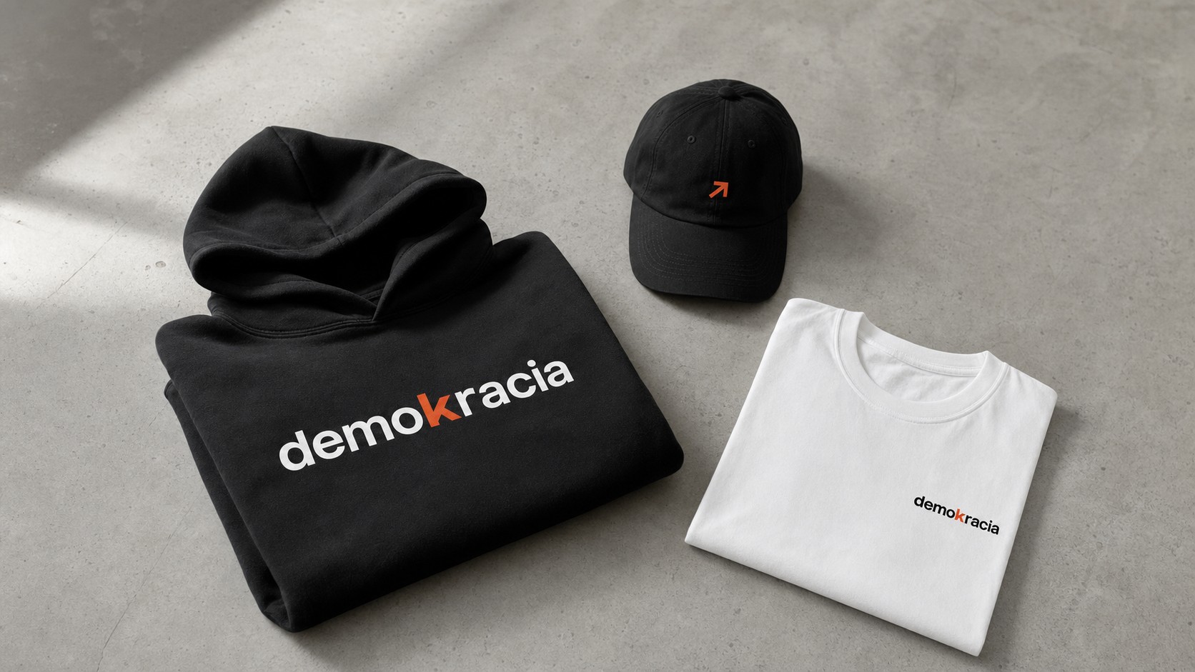 Flatlay de la colección Demokracia: sudadera, camiseta y gorra sobre superficie de hormigón